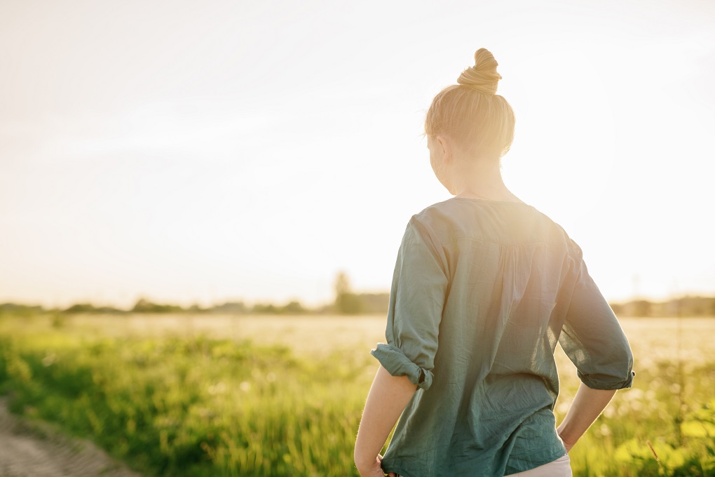 girl walking in field toward sunshine