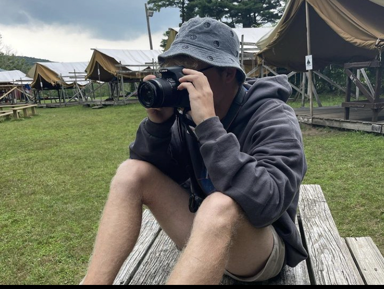 Young person Connor holding camera at camp
