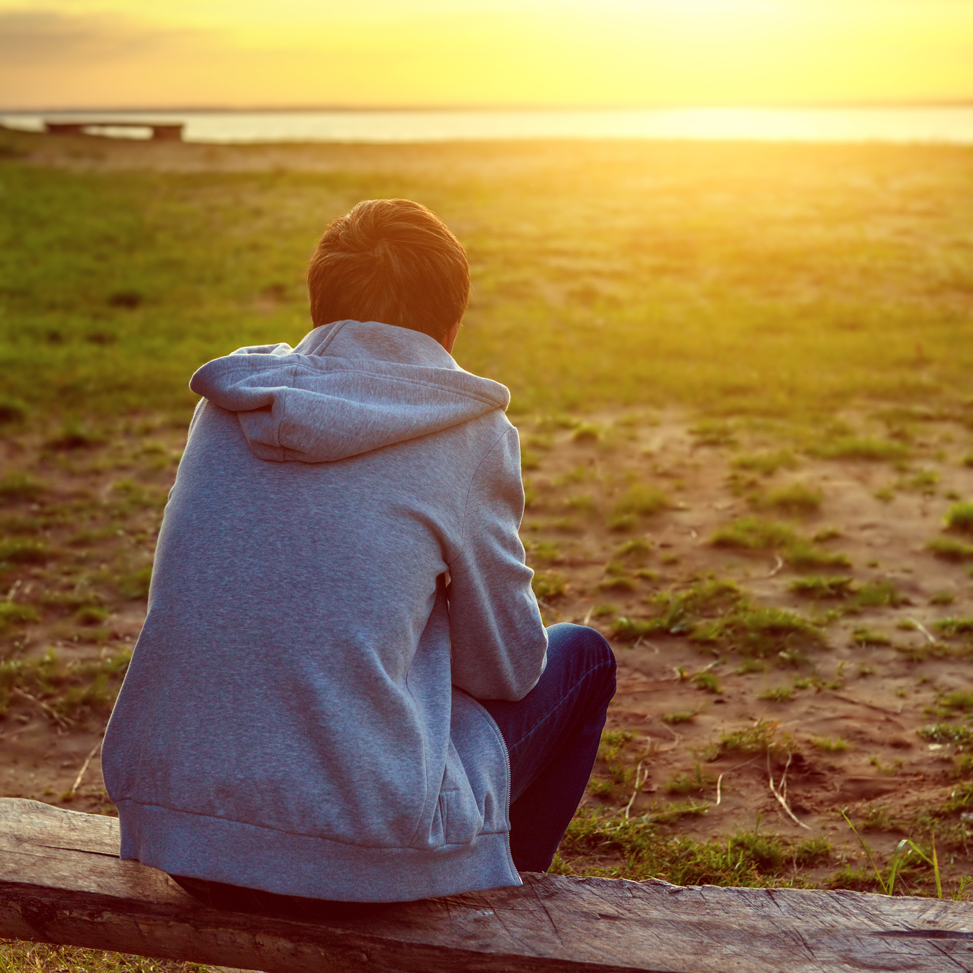 Boy sitting on bench looking across to sunset