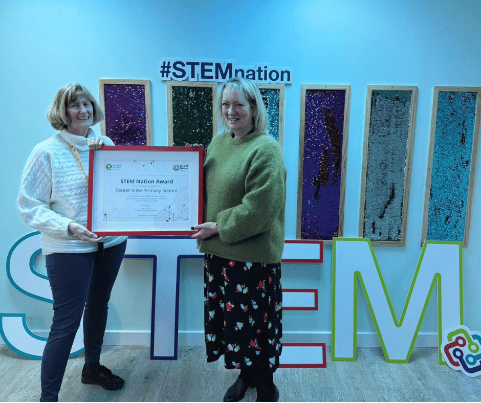 Two female staff holding certificate in front of a sign reading STEM